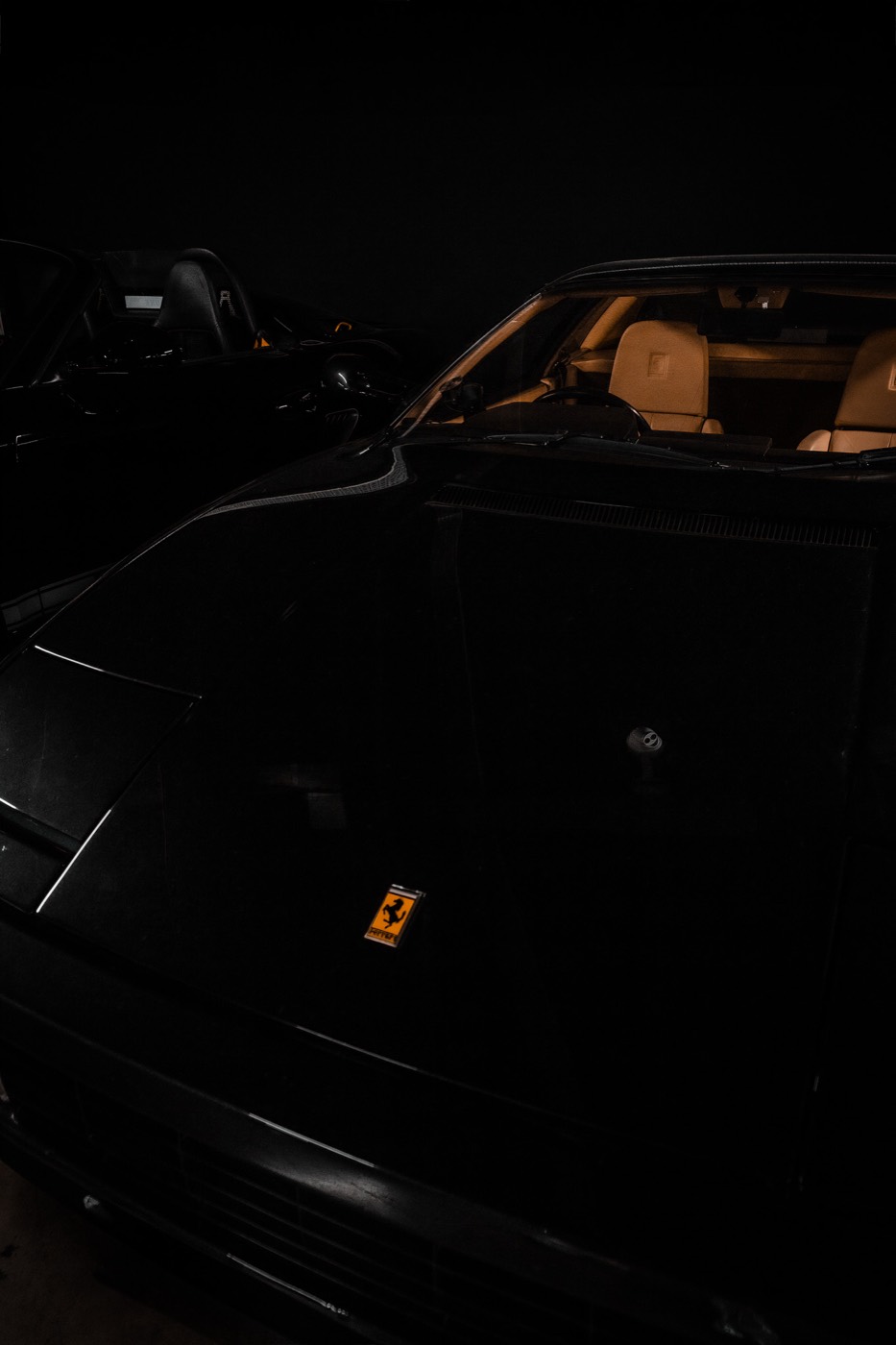 Dark showroom shot of a black Ferrari Testarossa with orange Ferrari badge, Duke of London